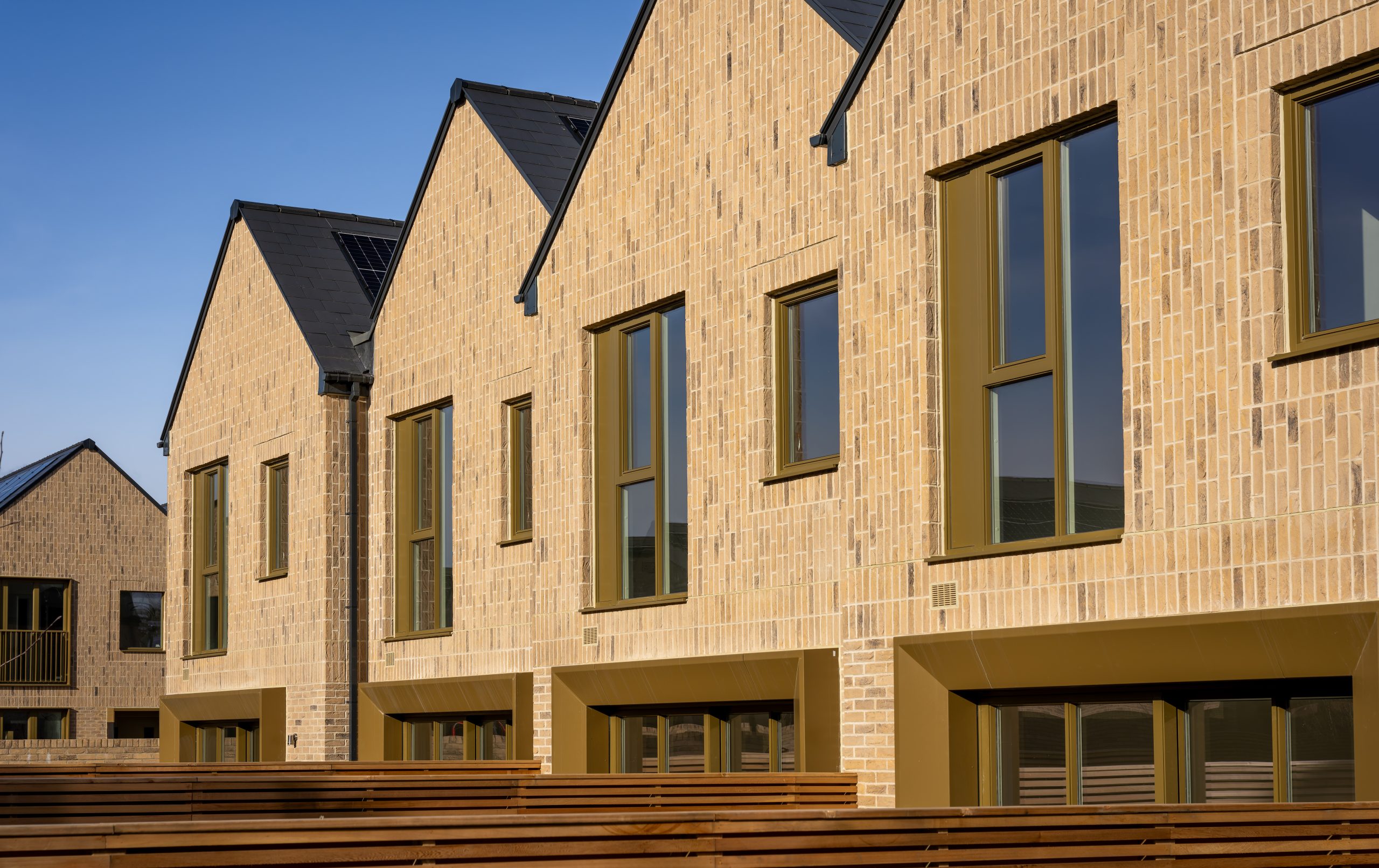 Close-up view of modern residential buildings with brick slip cladding, large windows, and pitched roofs at Eddington, Cambridge.